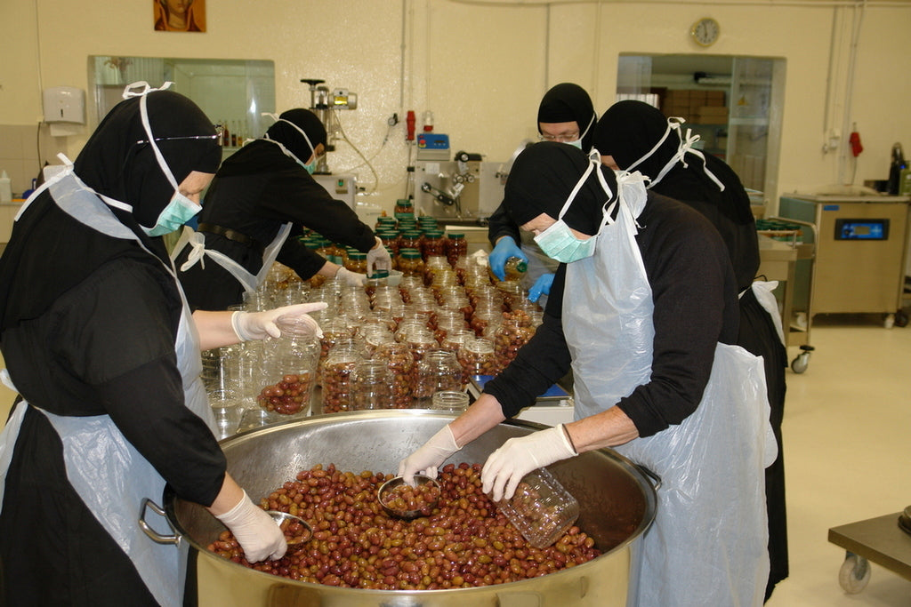 Nonnen im Kloster Ormylia verarbeiten Oliven. Mit Schutzkleidung und Masken füllen sie die Oliven in Gläser ab. Diese Szene zeigt die sorgfältige Handarbeit und die Herstellung hochwertiger, natürlicher Produkte in einem klösterlichen Umfeld.